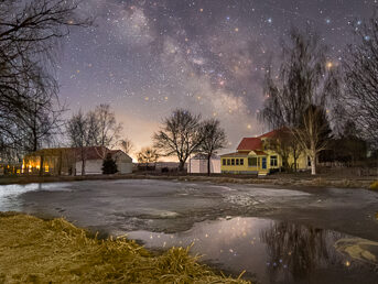 Milky Way Core and stars over a farmhouse and pond. The Milky Way reflects in the water of the pond